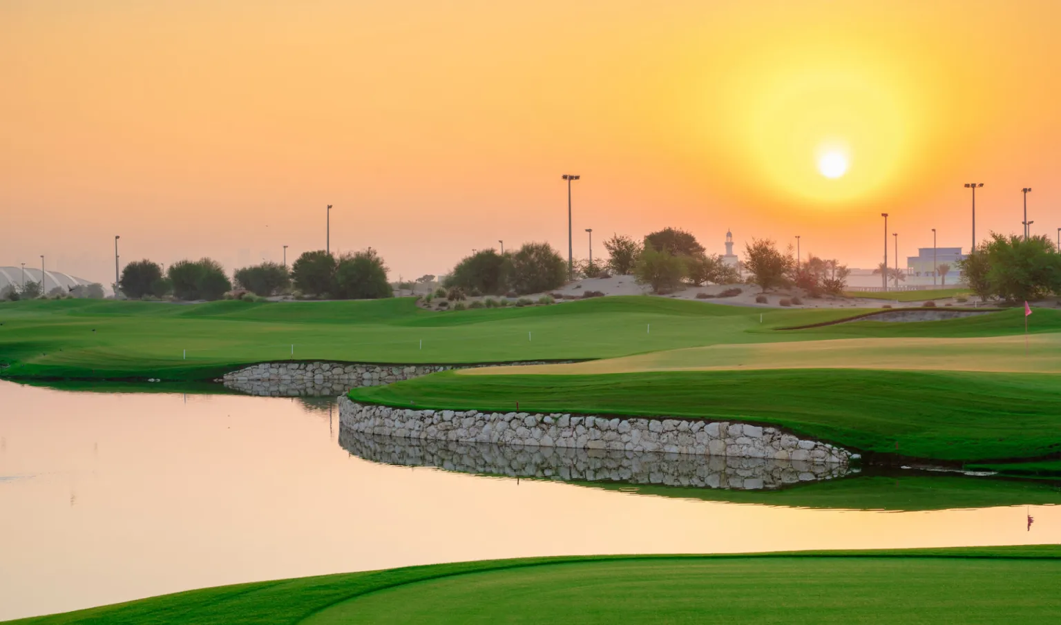 the sun is setting over a golf course with a pond.