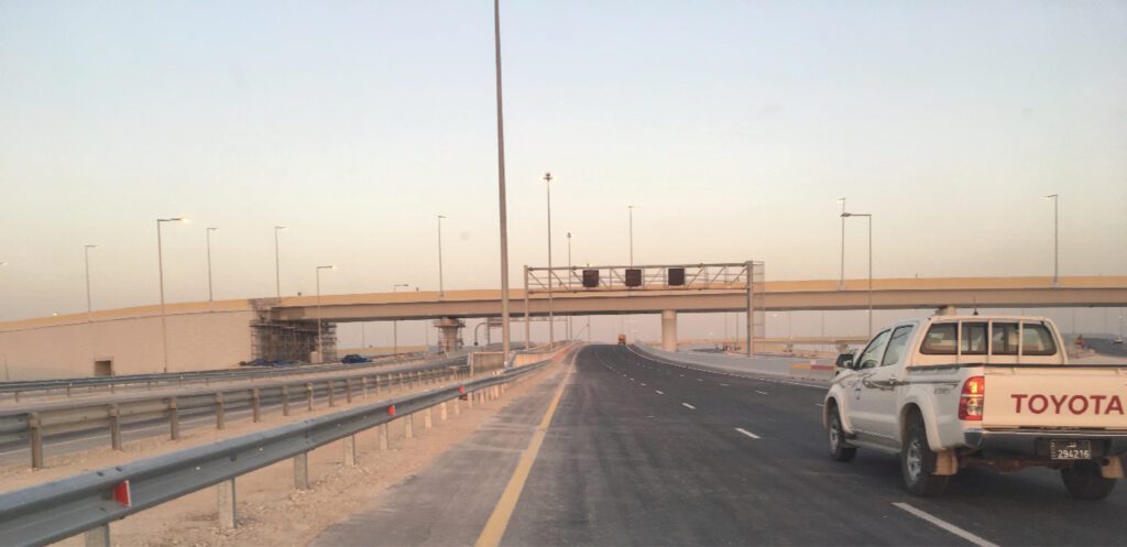a truck driving down a highway with a bridge in the background.