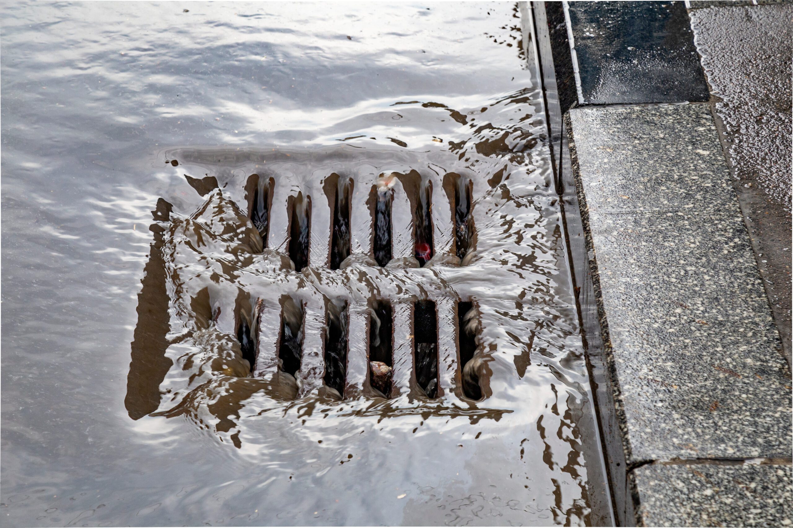 a manhole with a drain in the middle of a flooded street.