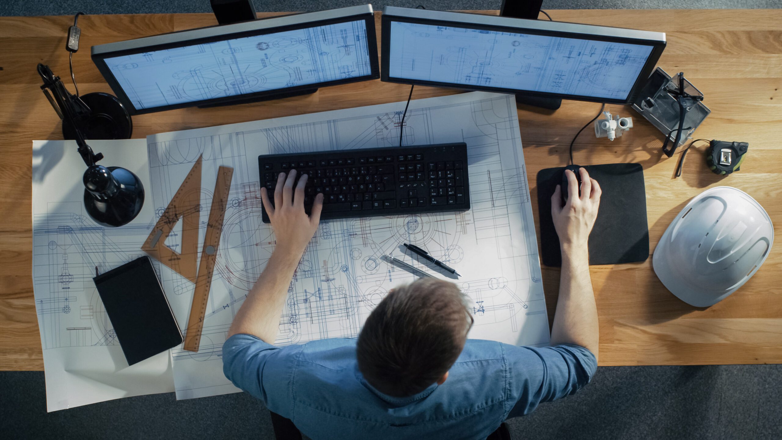 a man working at a desk with blueprints and a computer.